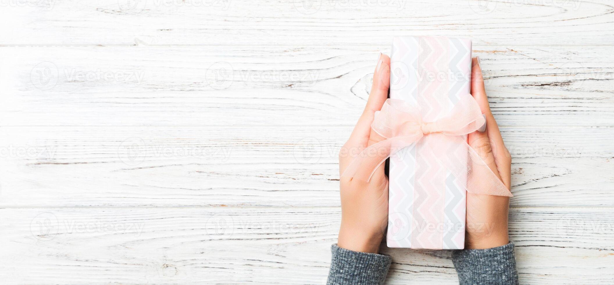 Female hands holding present on white rustic wooden background. Festive backdrop for Christmas holidays or other holiday . Flat lay style top view with copy space photo