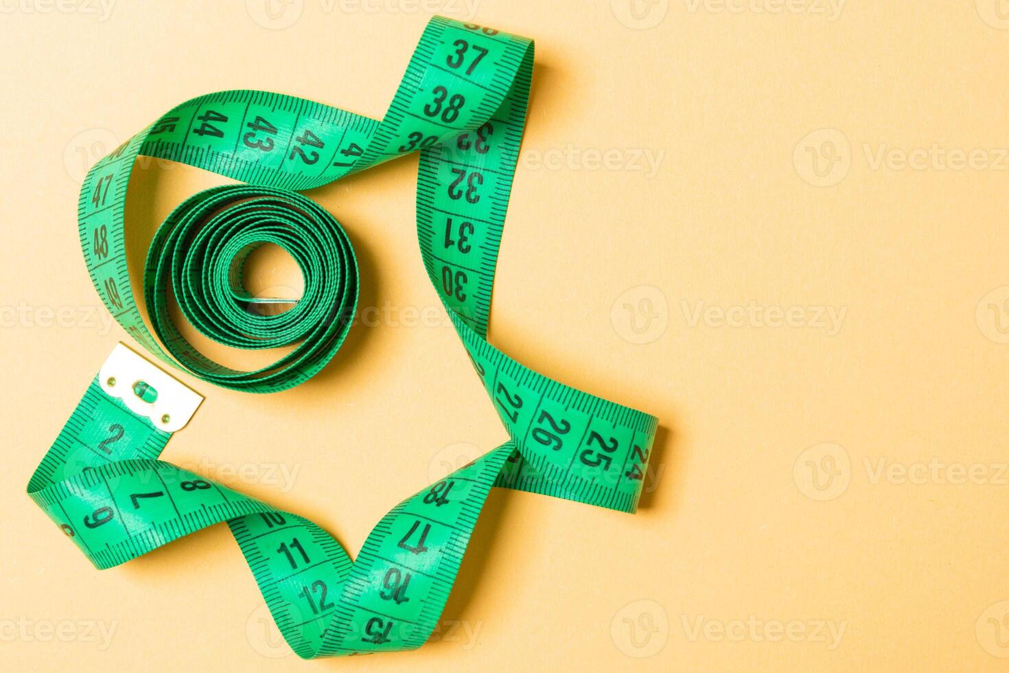 Top view of measure tape curtailed into a spiral with copy space. Concept of sewing accessory or healthy diet on orange background photo