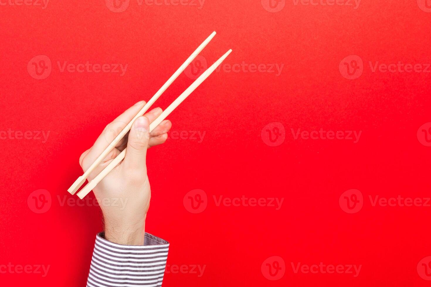 Male hand with chopsticks on red background. Traditional asian food with emty space for your design photo