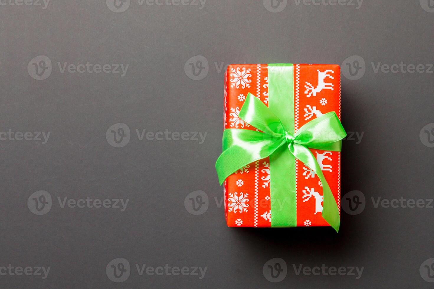 wrapped Christmas or other holiday handmade present in paper with green ribbon on black background. Present box, decoration of gift on colored table, top view with copy space photo