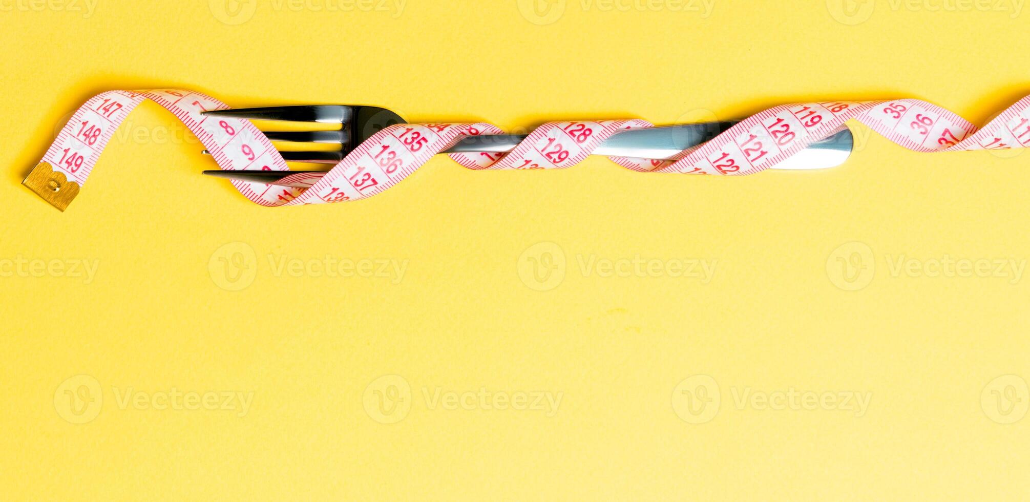 Composition of curled wrapped measuring tape and fork on yellow background. Overweight concept photo