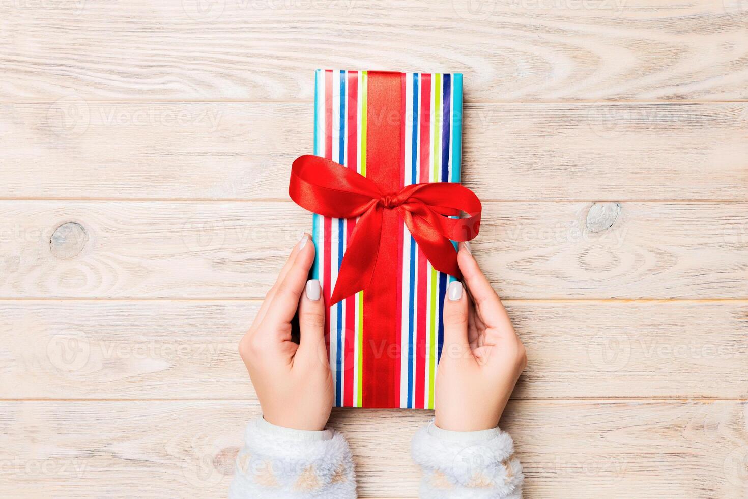 Woman hands give wrapped christmas or other holiday handmade present in colored paper . Present box, decoration of gift on yellow rustic wooden table, top view with copy space photo