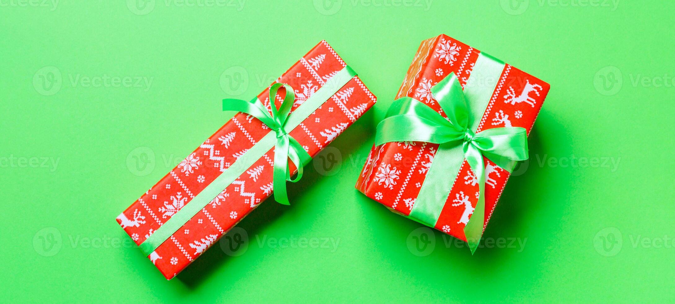 wrapped Christmas or other holiday handmade present in paper with green ribbon on green background. Present box, decoration of gift on colored table, top view photo