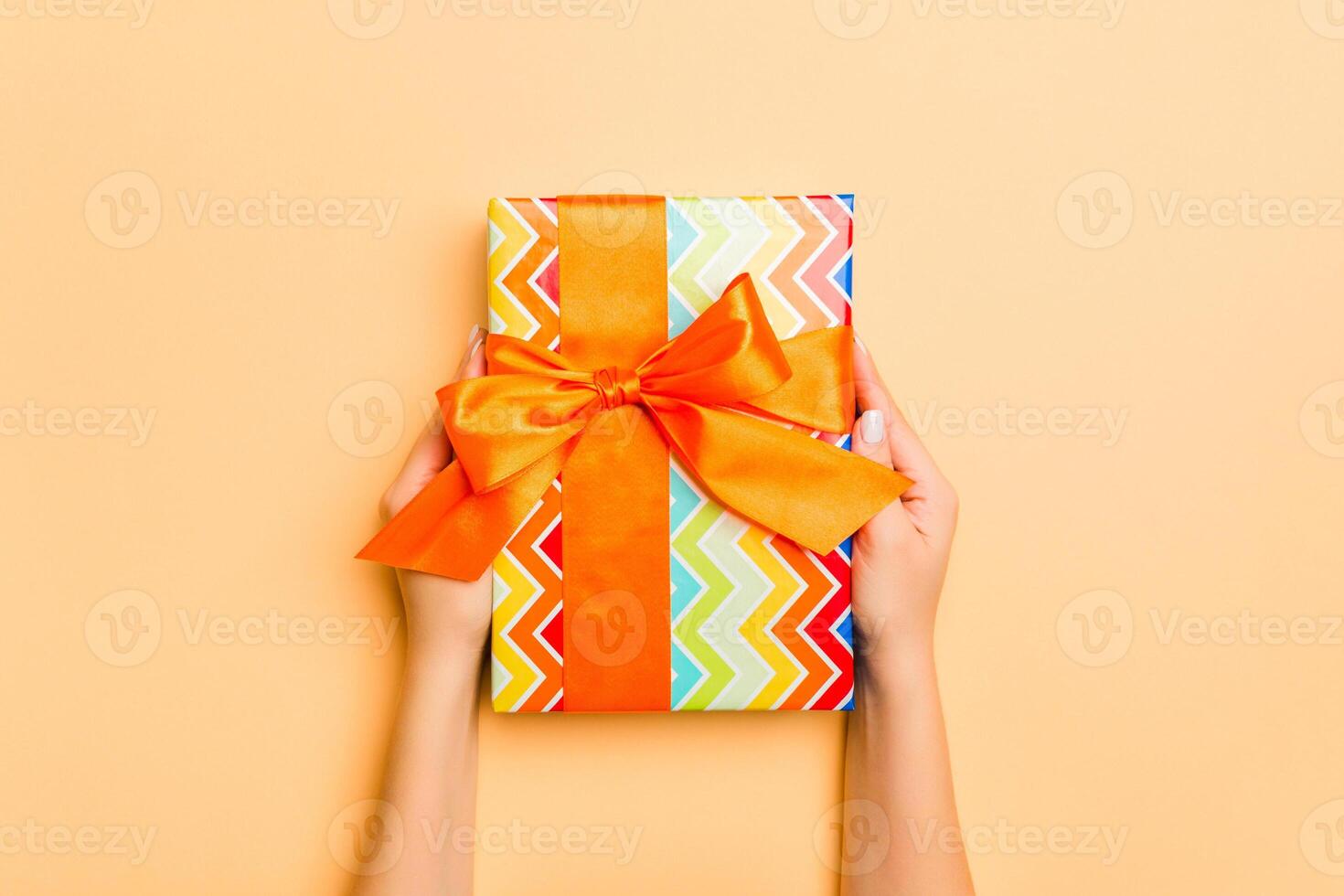 Flat lay of woman hands holding gift wrapped and decorated with bow on gold background with copy space. Christmas and holiday concept photo