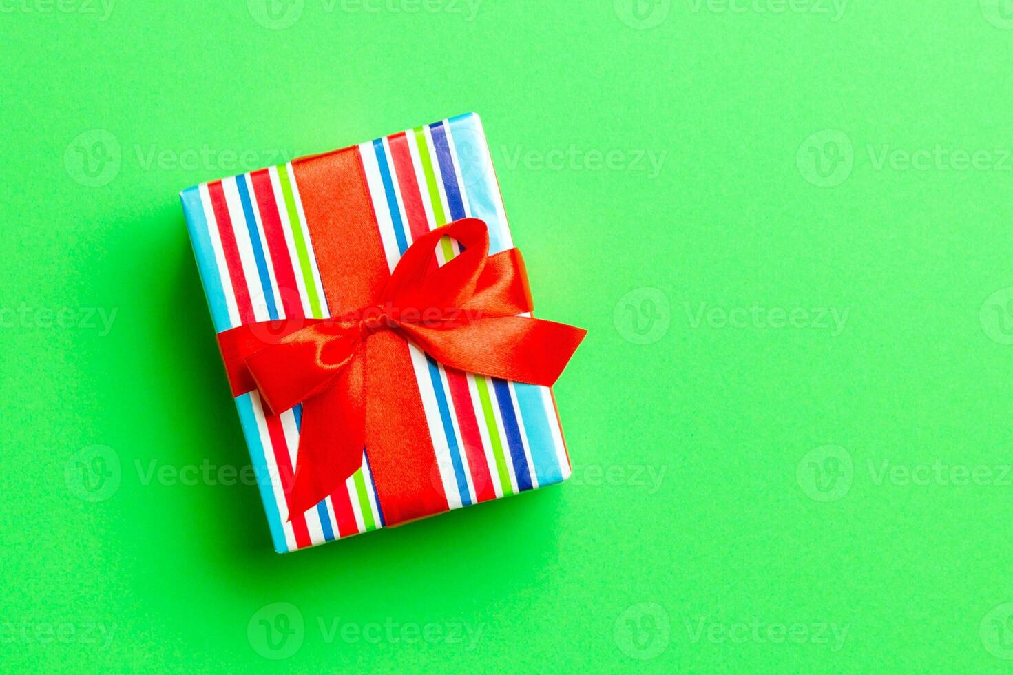 wrapped Christmas or other holiday handmade present in paper with red ribbon on green background. Present box, decoration of gift on colored table, top view with copy space photo