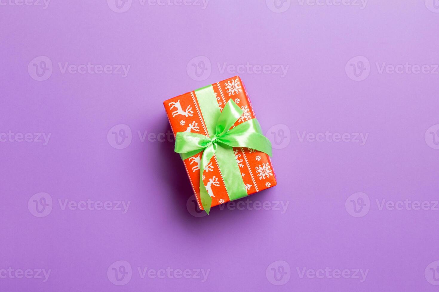 Gift box with green bow in hands for Christmas or New Year day on purple background, top view with copy space photo