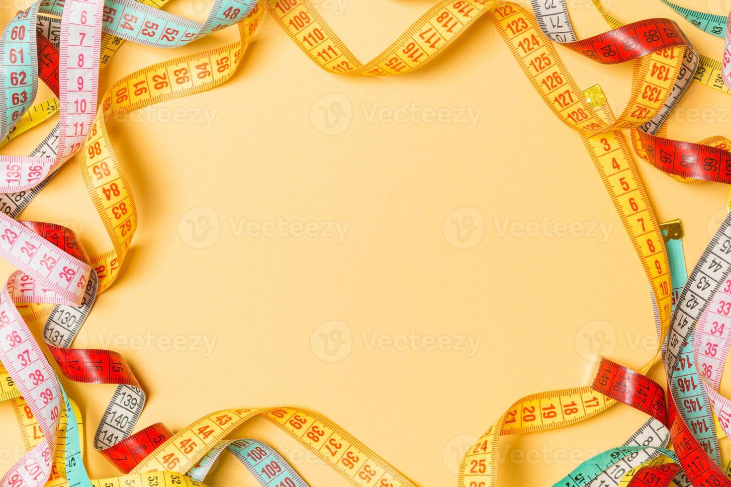 Heap of colorful measuring tapes in the form of frame on orange background. Top view of slim waist concept with copy space photo