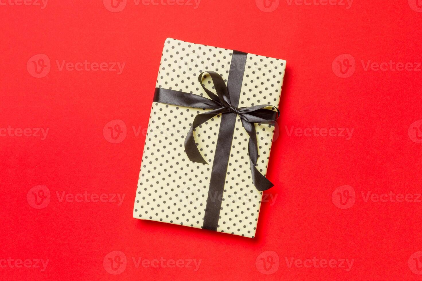 Gift box with black bow for Christmas or New Year day on red background, top view with copy space photo