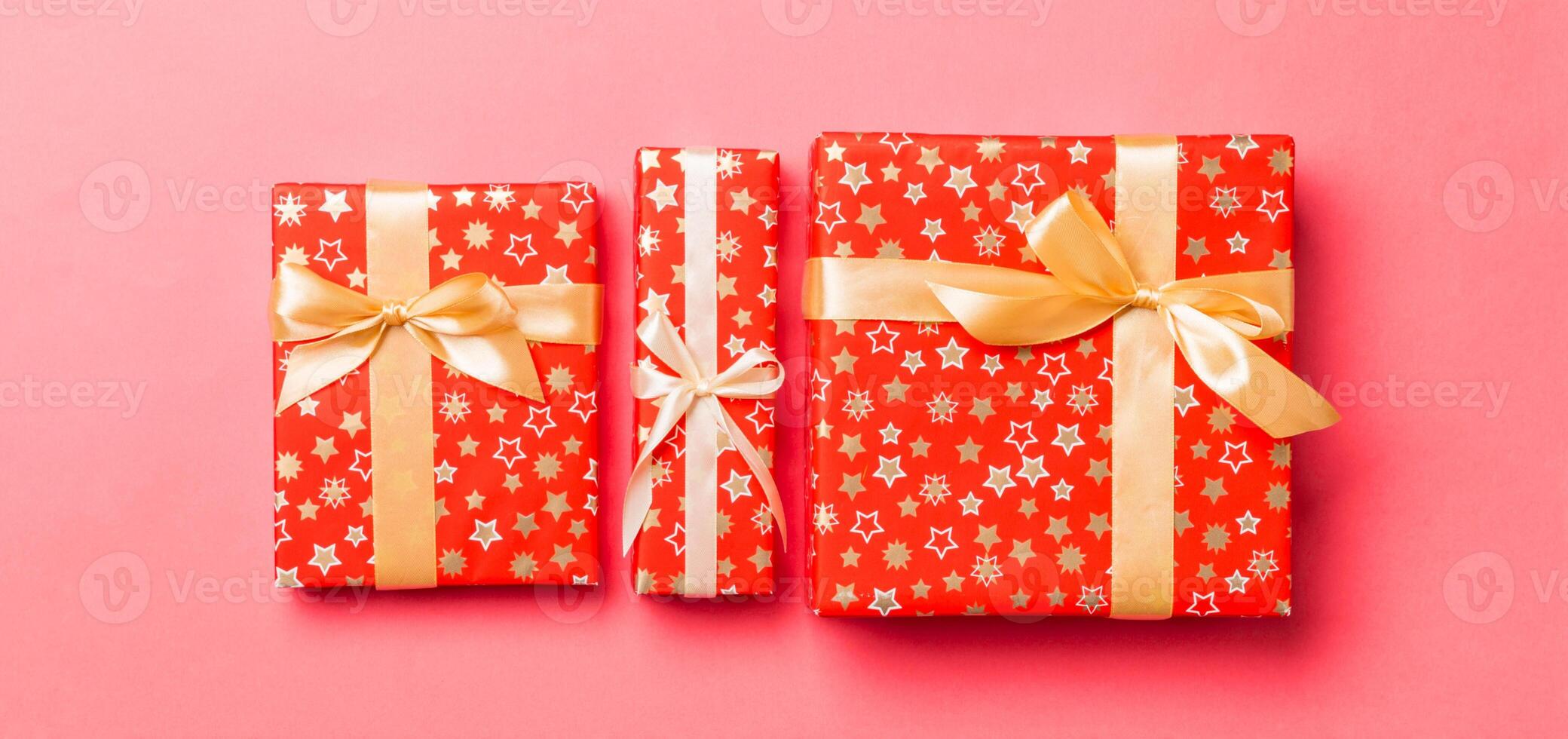 wrapped Christmas or other holiday handmade present in paper with gold ribbon on living coral background. Present box, decoration of gift on colored table, top view photo