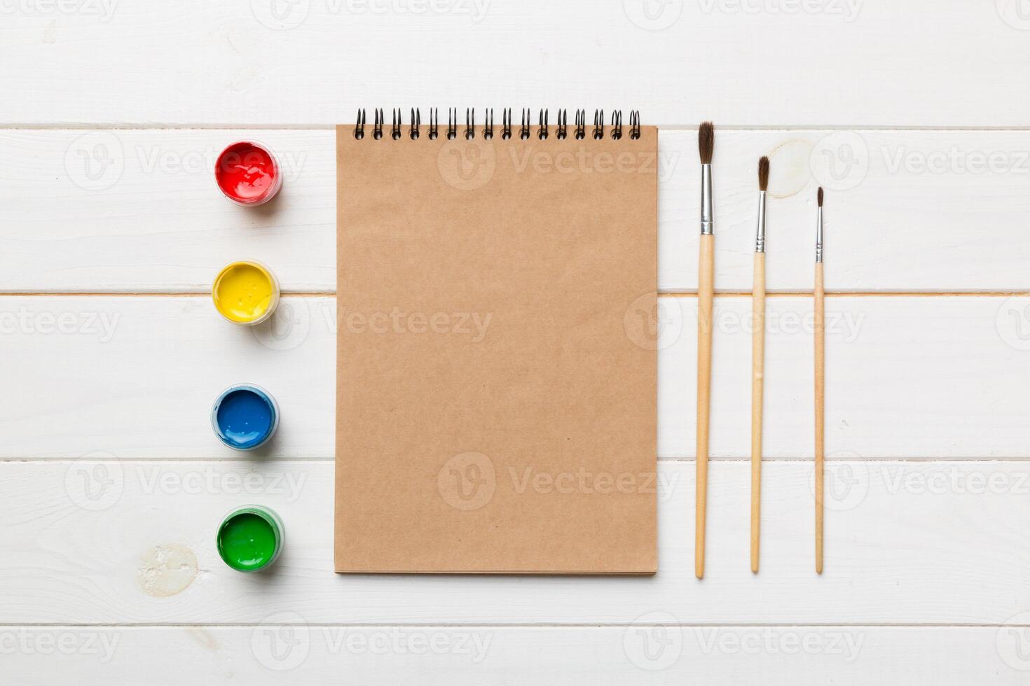 Album pages and paints, pencils, brush on a colored background. Top view with empty space. workplace for creativity. home teaching concept drawing photo