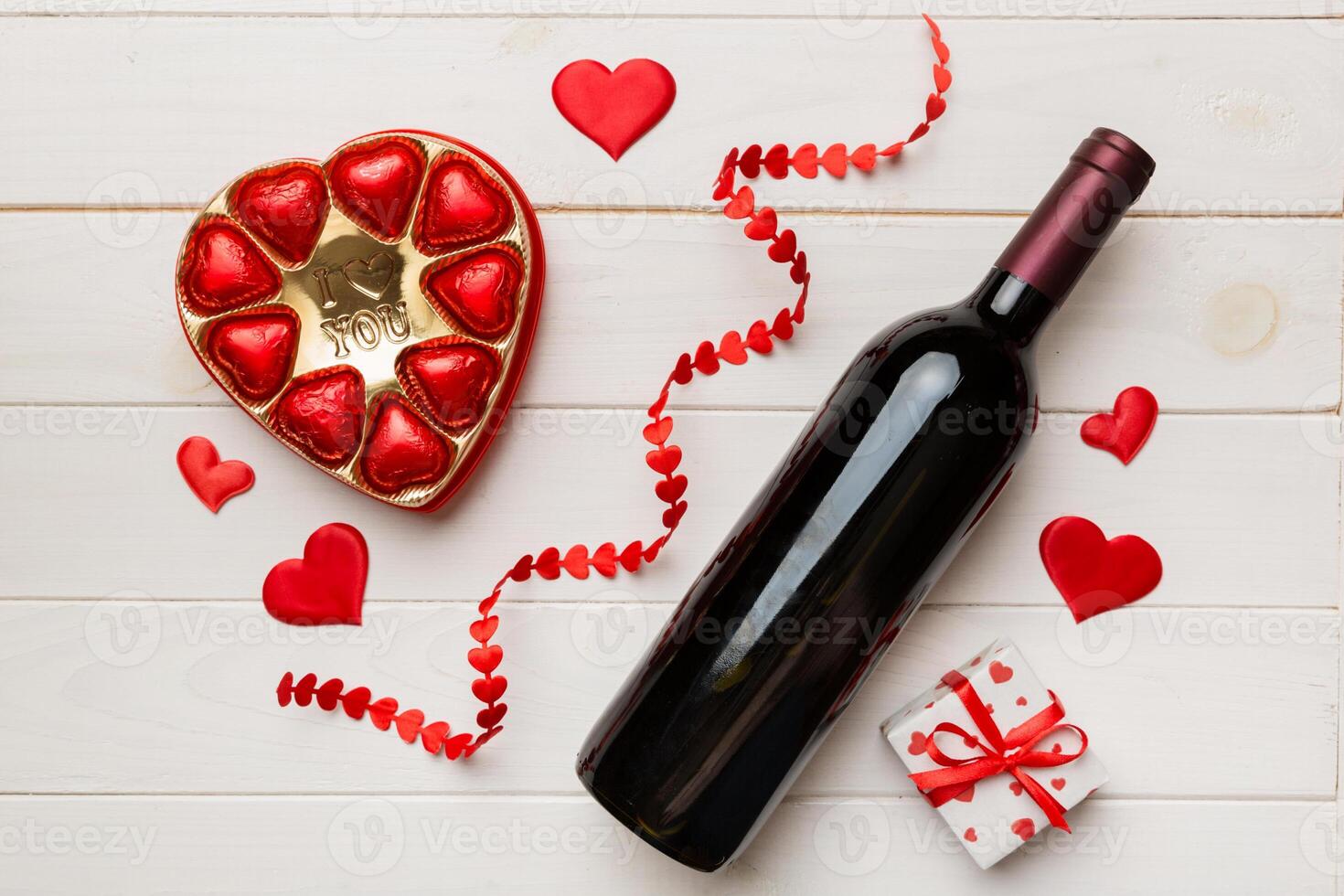 Bottle of red wine on colored background for Valentine Day with gift and chocolate. Heart shaped with gift box of chocolates top view with copy space photo