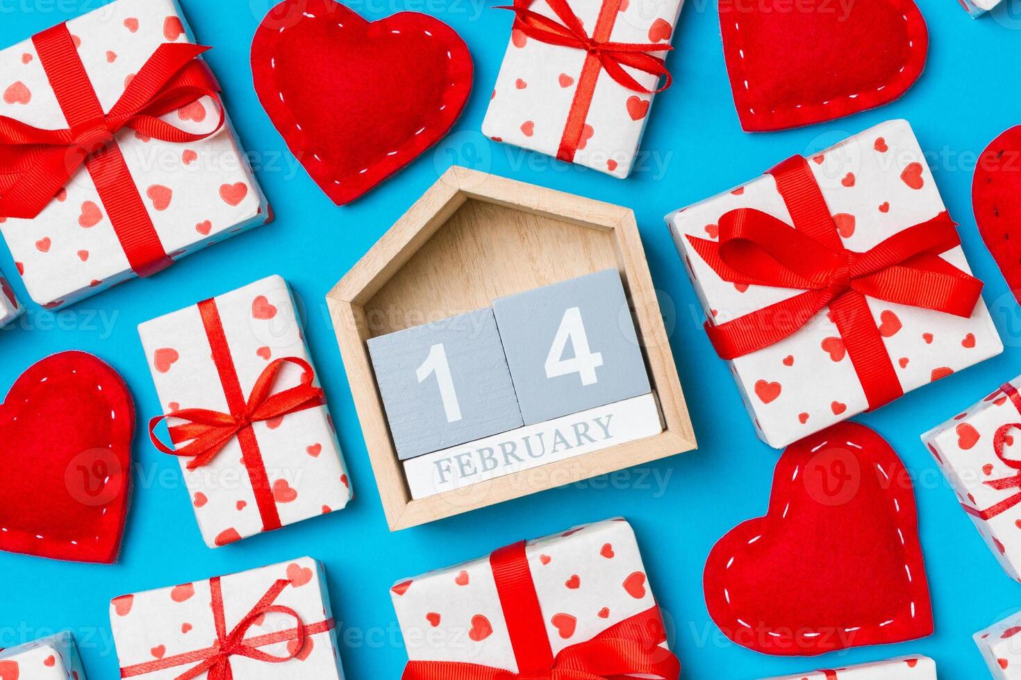 Top view of wooden calendar, white gift boxes and red textile hearts on colorful background. Valentine's Day concept photo