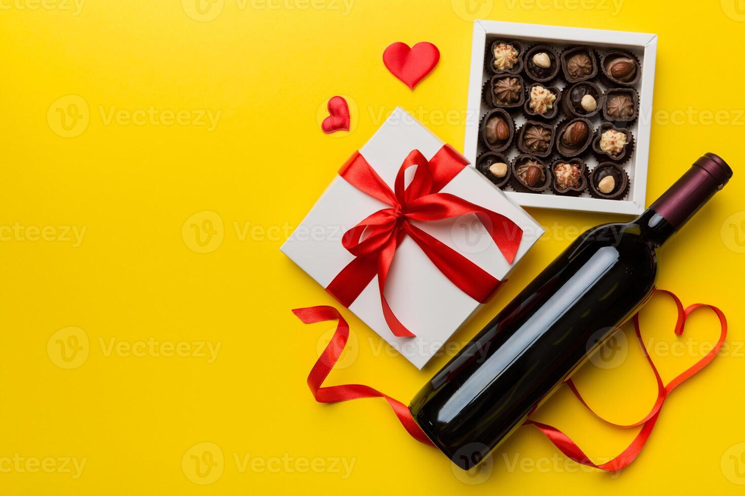 Bottle of red wine on colored background for Valentine Day with gift and chocolate. Heart shaped with gift box of chocolates top view with copy space photo