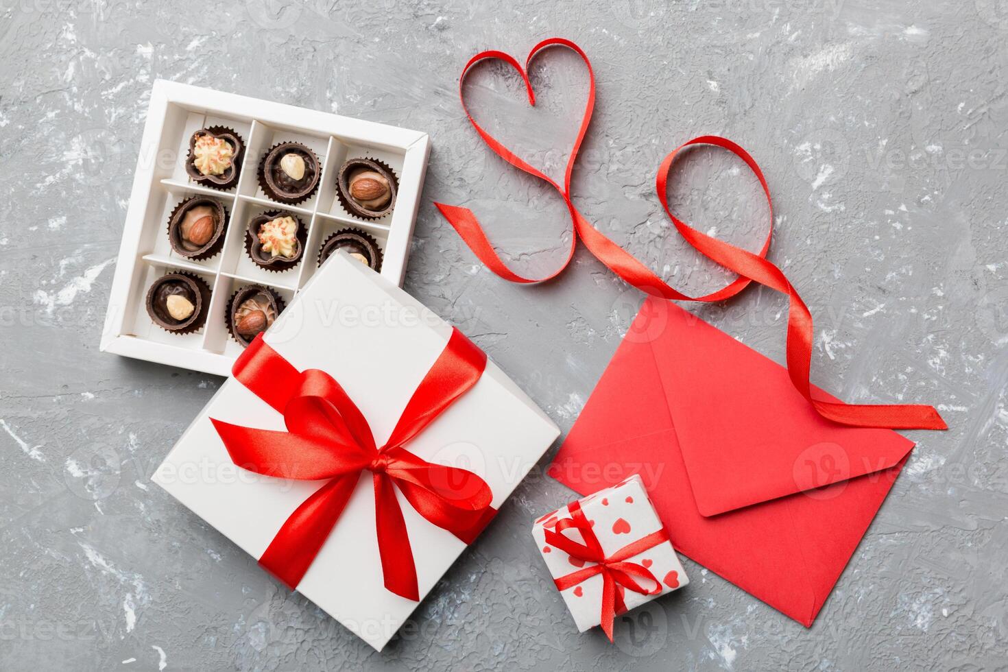 Envelope on colored background for Valentine Day with gift box and chocolate. Heart shaped with gift box of chocolates top view with copy space photo