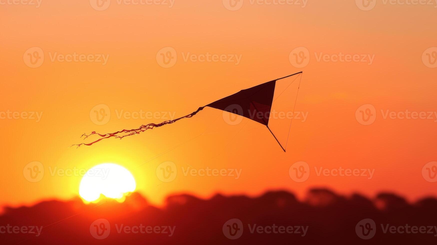 The sun setting behind a silhouette of trees a single kite with a long streaming tail flying against the orange and pink sky photo