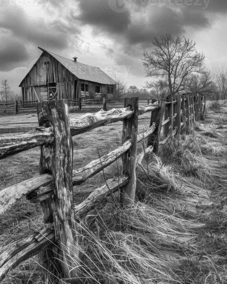 The barns weathered wooden fence has long since fallen into disrepair a reminder of a time long gone. Black and white art. photo