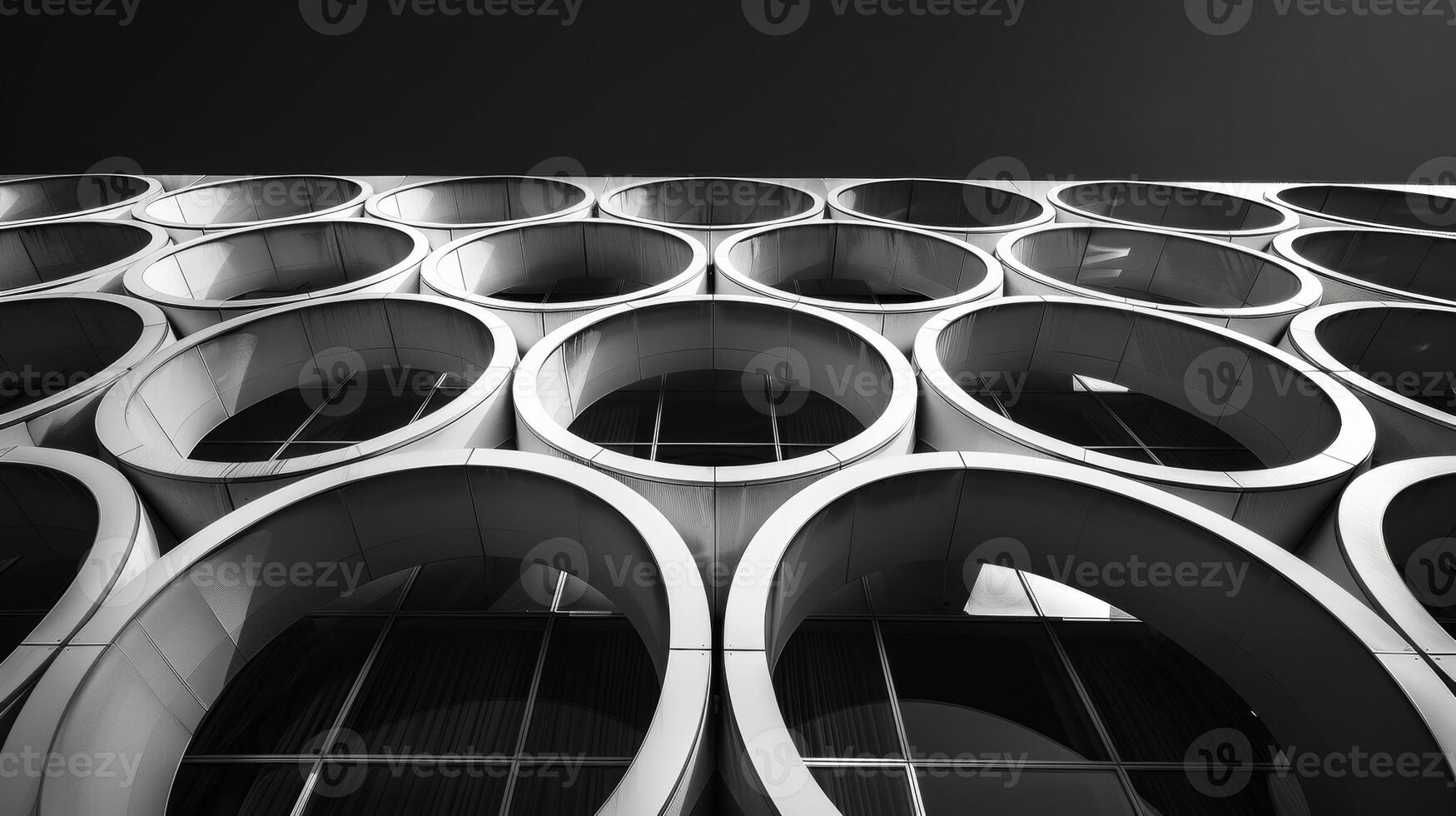 The repeating patterns of a series of spherical windows on a steel building create a mesmerizing visual effect against the black sky. Black and white art. photo