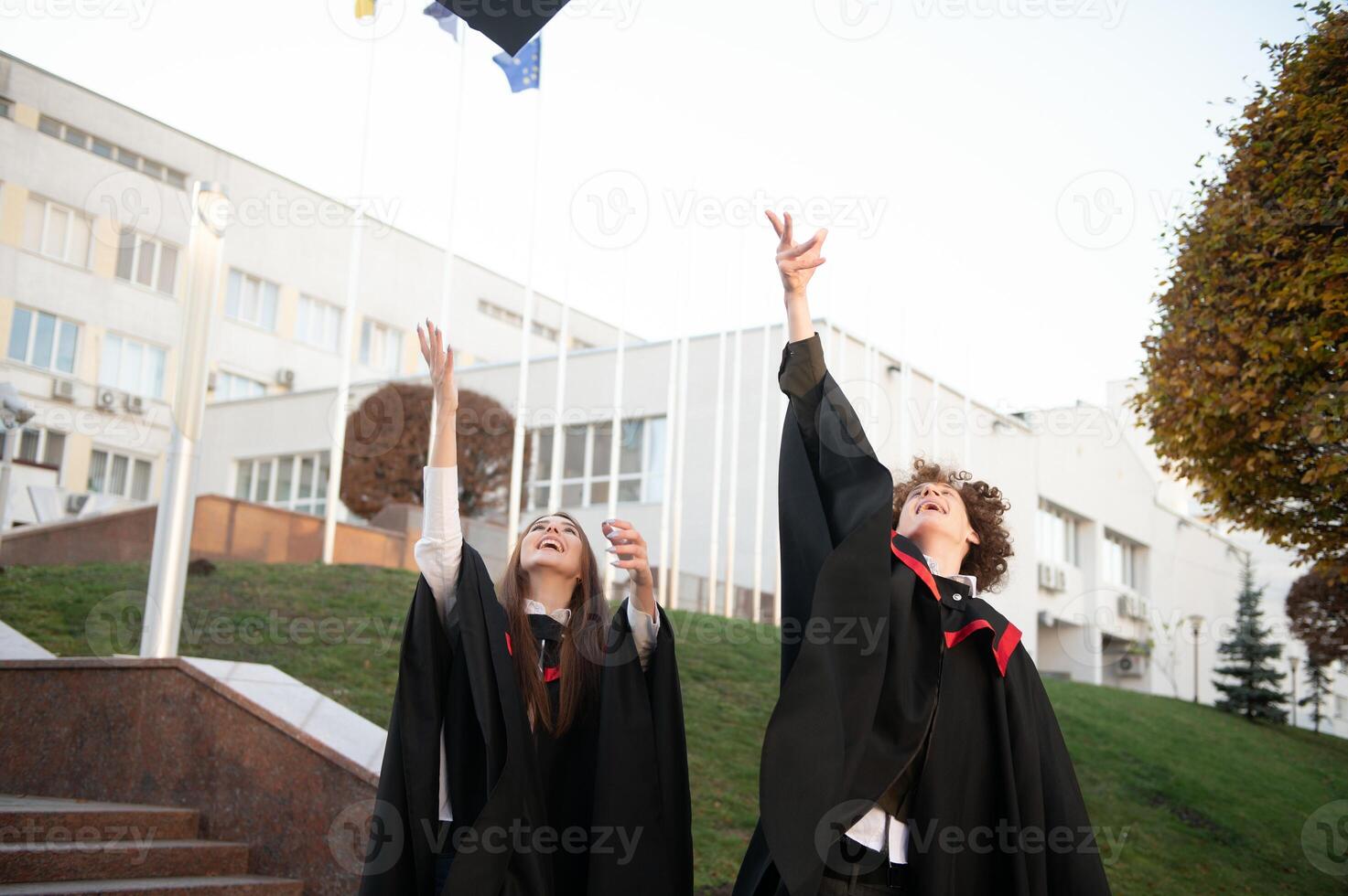 Graduates in mantles with diplomas in hands are standing near university. photo