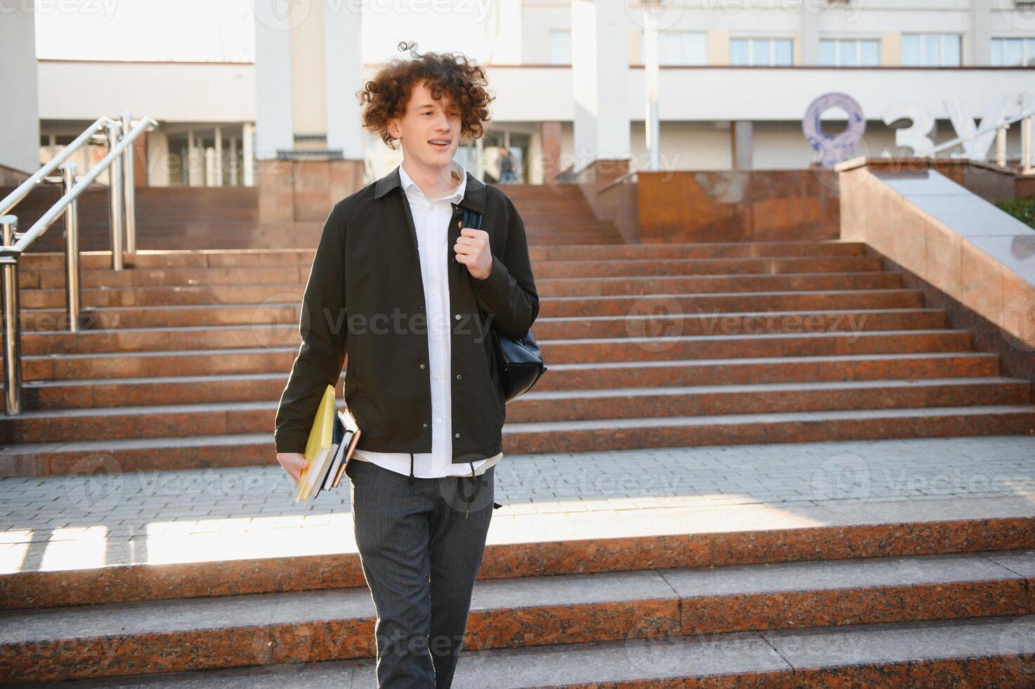 Happy handsome university, college student or young smart successful guy, school pupil with books textbooks smiling outdoors at sunset. Copy space photo