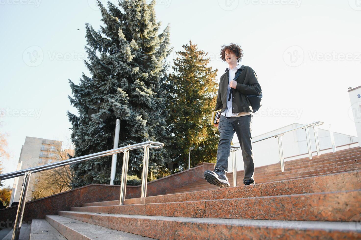 Happy handsome university, college student or young smart successful guy, school pupil with books textbooks smiling outdoors at sunset. Copy space photo