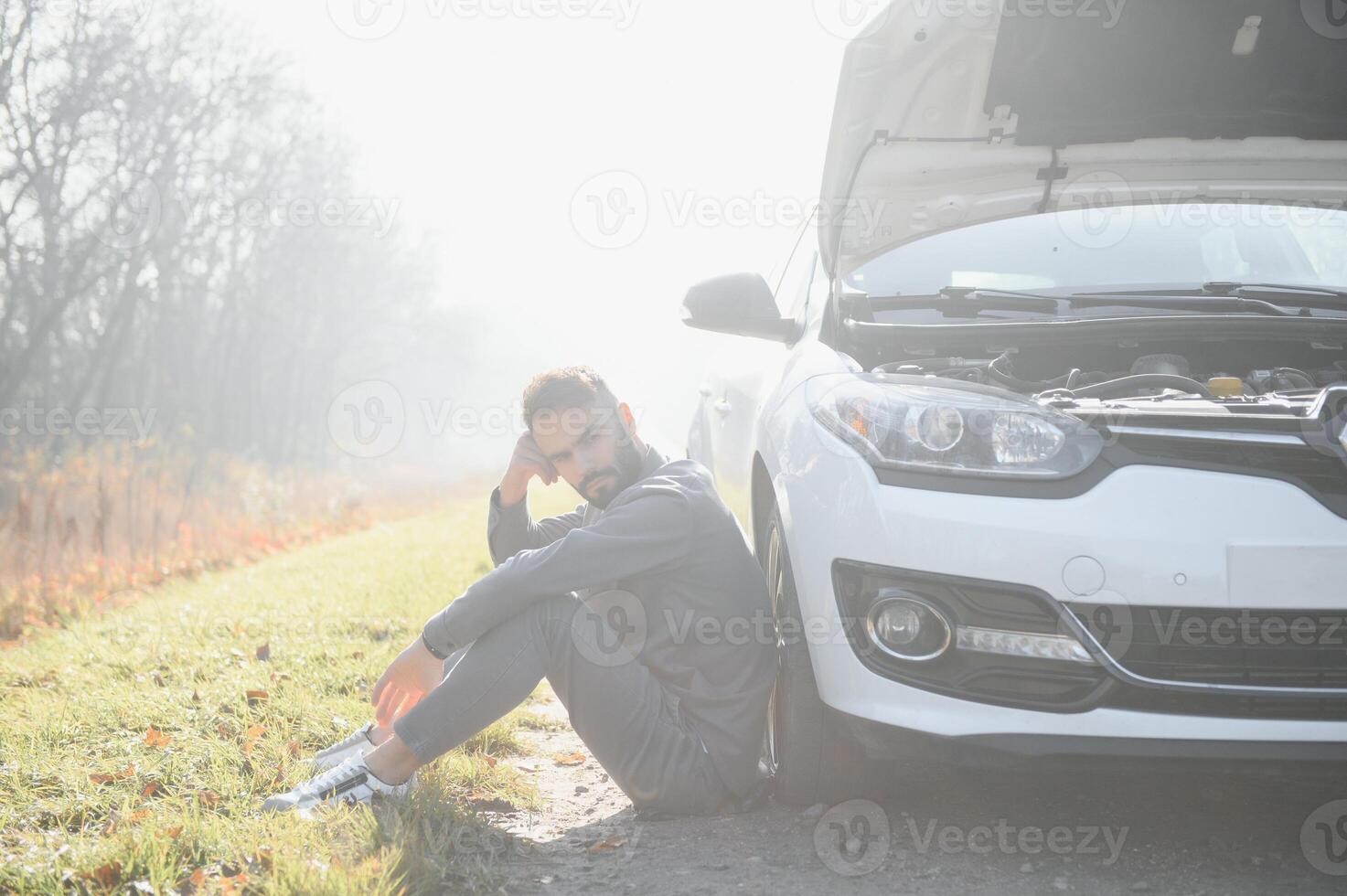 Sad driver holding his head having engine problem standing near broken car on the road. Car breakdown concept photo