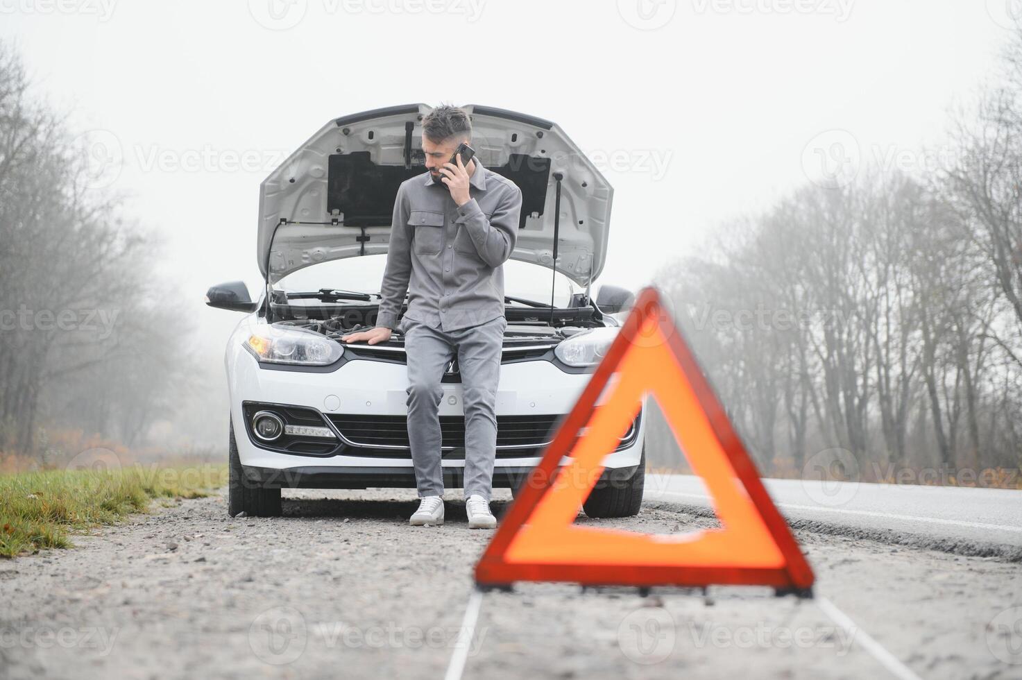 Man use a cellphone call garage in front of the open hood of a broken car on the road in the forest. Car breakdown concept. photo