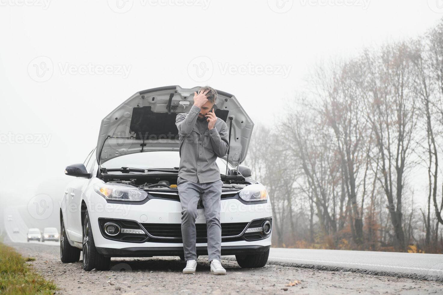 Man use a cellphone call garage in front of the open hood of a broken car on the road in the forest. Car breakdown concept. photo