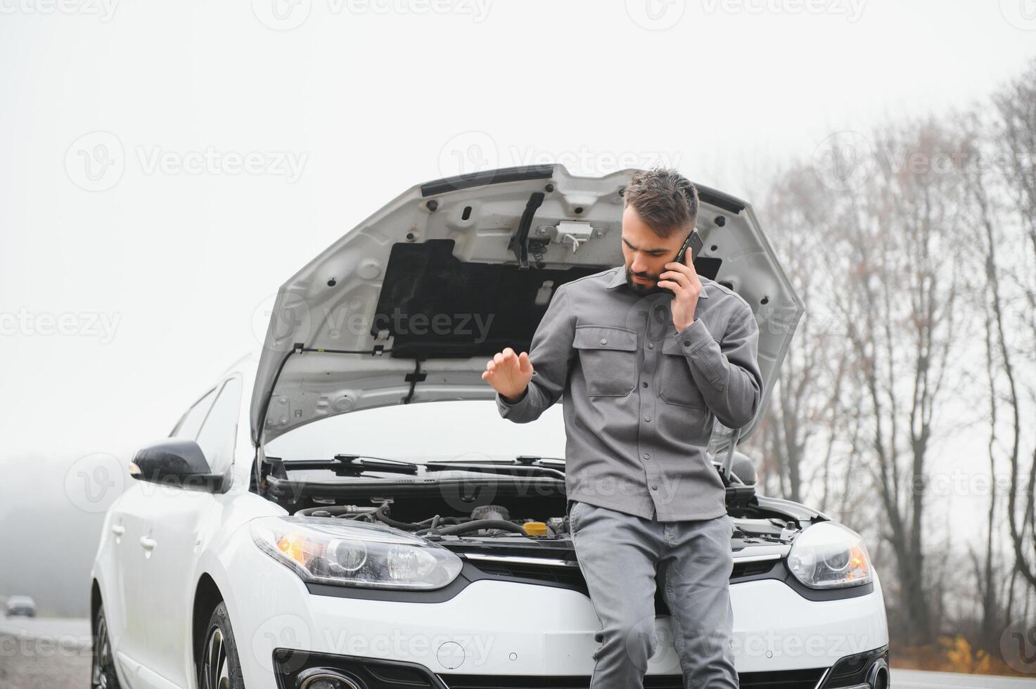 Man use a cellphone call garage in front of the open hood of a broken car on the road in the forest. Car breakdown concept. photo