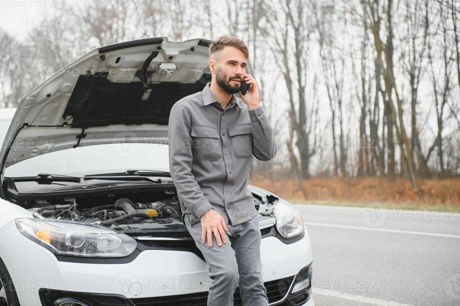 Sad driver calling car service, opening hood, having engine problem standing near broken car on the road. Car breakdown concept photo