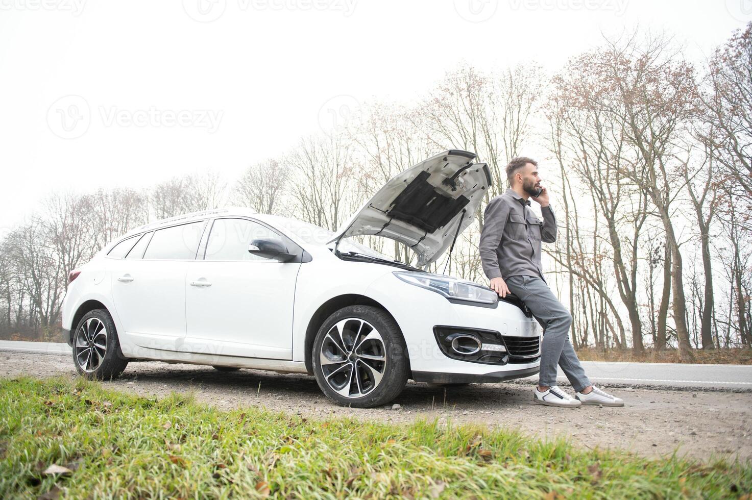 Man use a cellphone call garage in front of the open hood of a broken car on the road in the forest. Car breakdown concept. photo