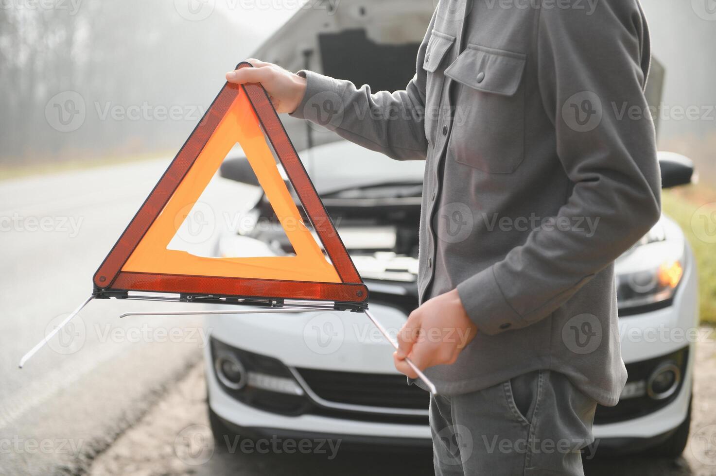 A young man near a broken car with an open hood on the roadside. photo