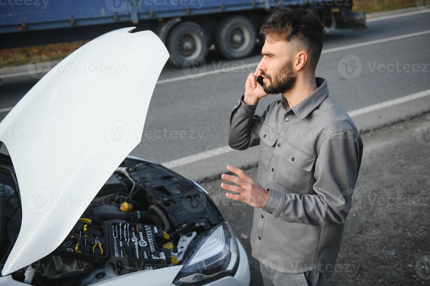 Sad driver calling car service, opening hood, having engine problem standing near broken car on the road. Car breakdown concept photo