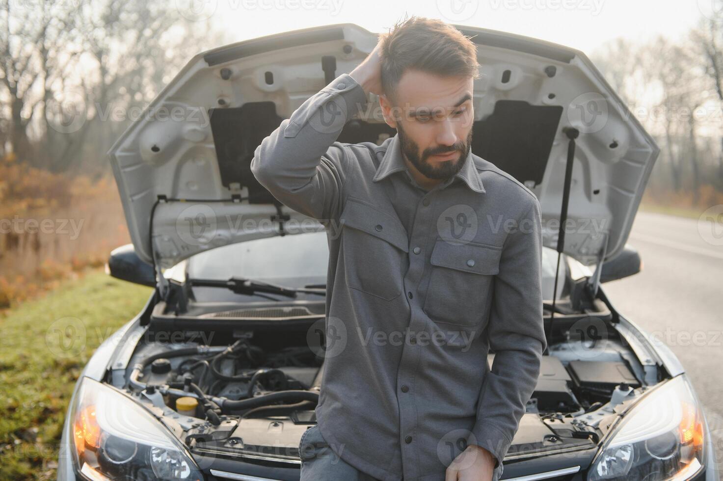 Sad driver holding his head having engine problem standing near broken car on the road. Car breakdown concept photo