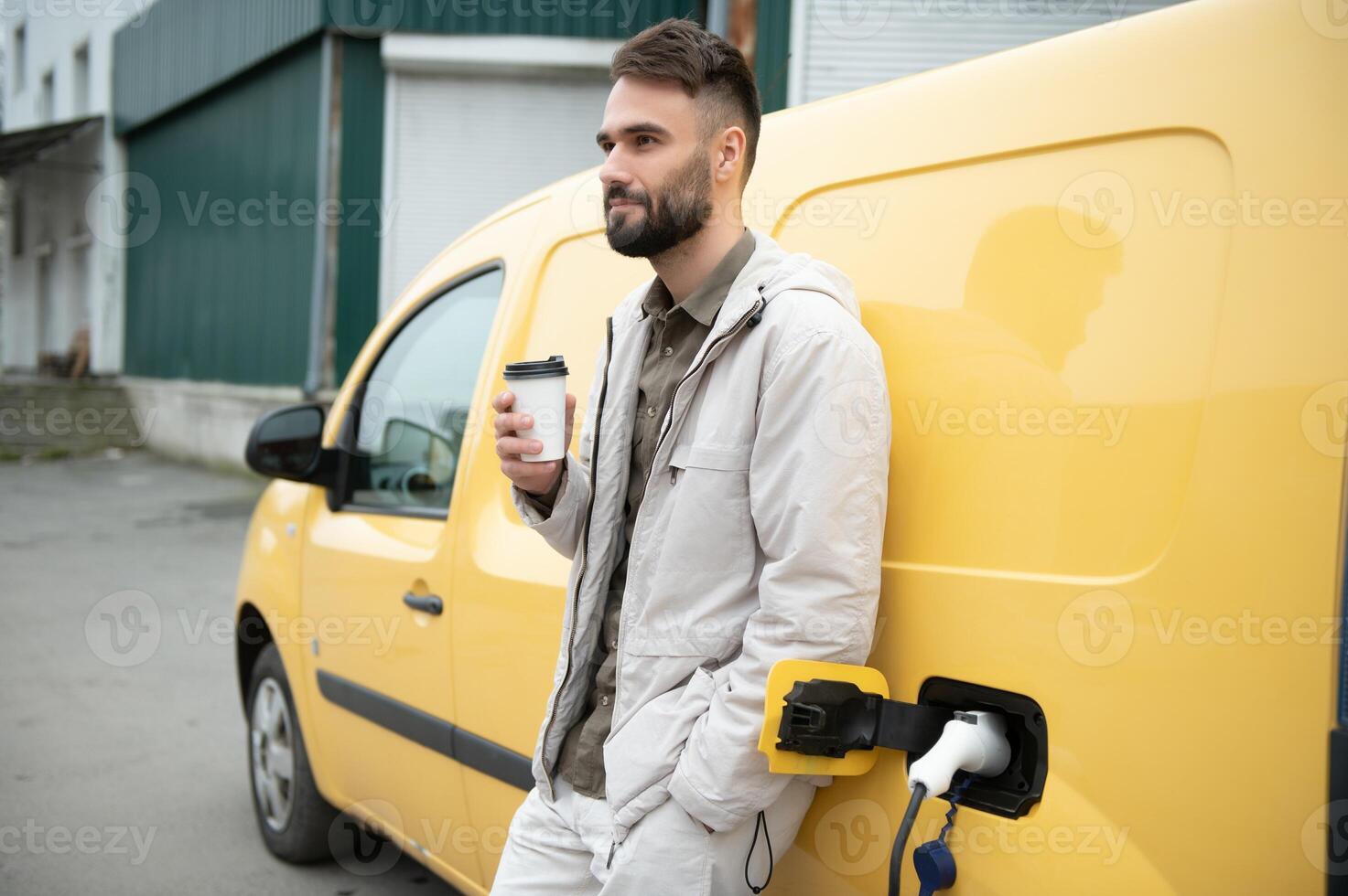 Handsome man drinking coffee while charging electric car photo