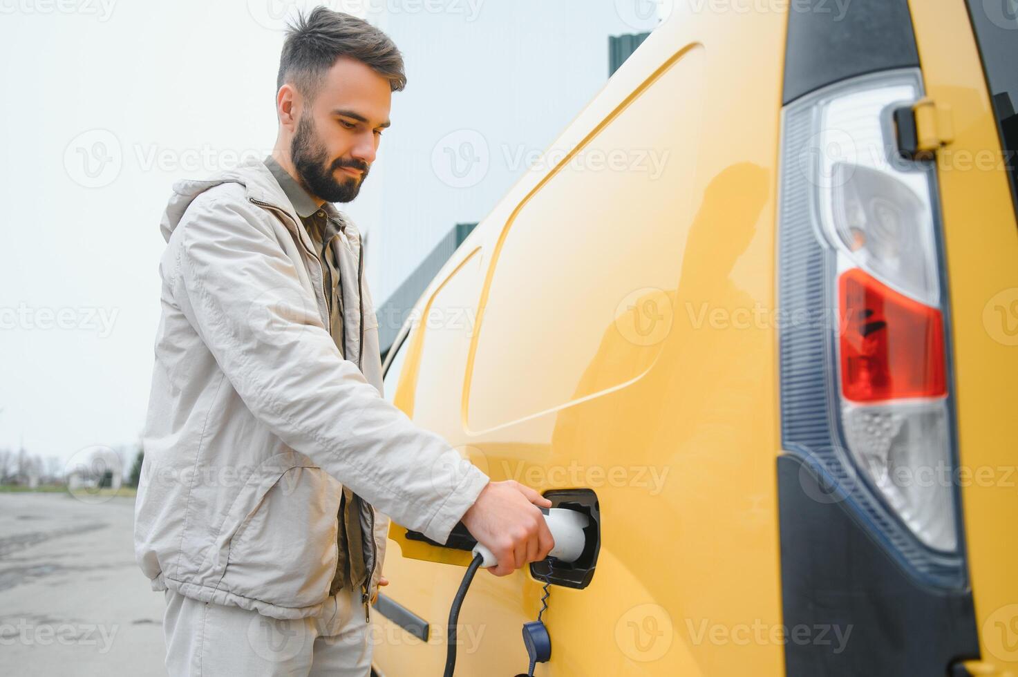 Portrait of a young man standing with charging cable near the charging station photo