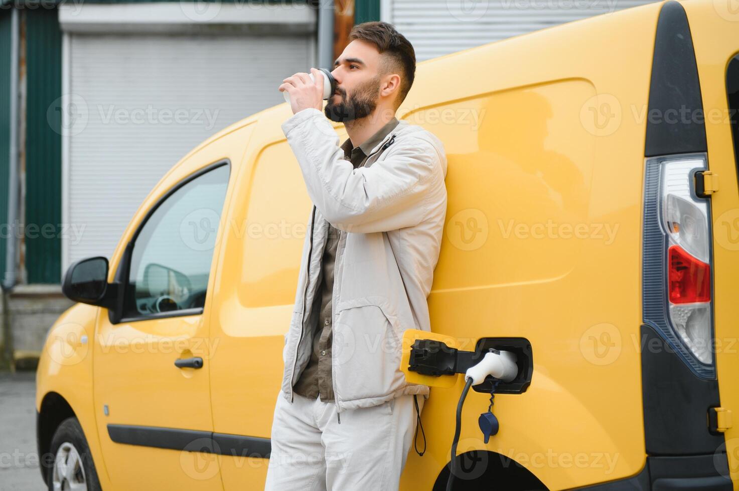 Handsome man drinking coffee while charging electric car photo