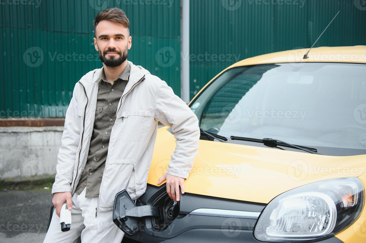 Man Holding Power Charging Cable For Electric Car In Outdoor Car Park. And he s going to connect the car to the charging station in the parking lot near the shopping center photo