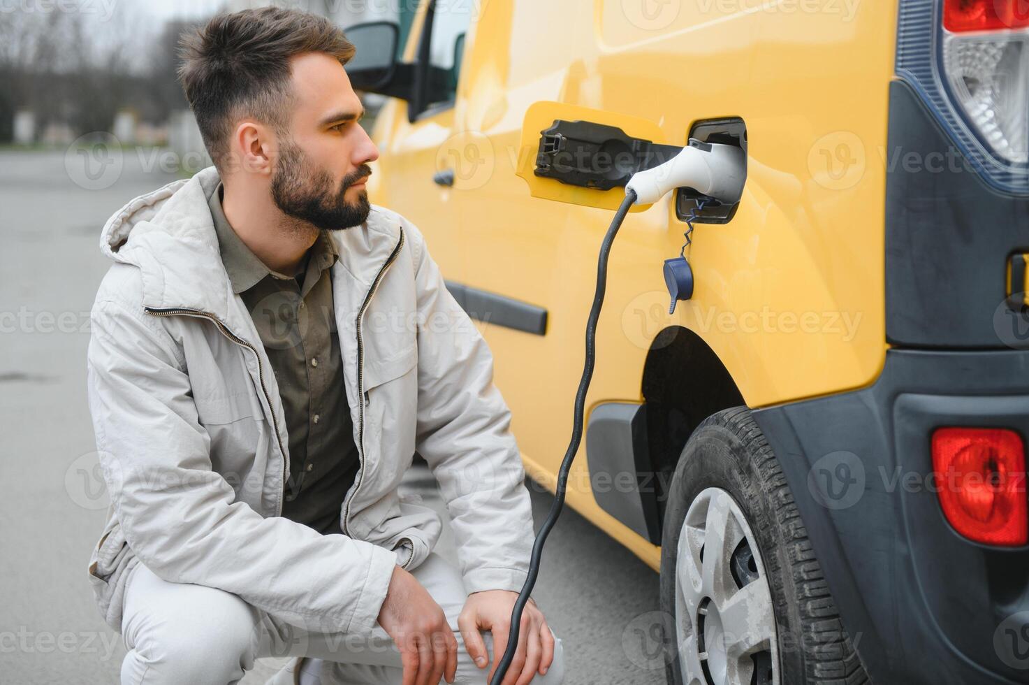 Casual man near electric car waiting for the finish of the battery charging process photo