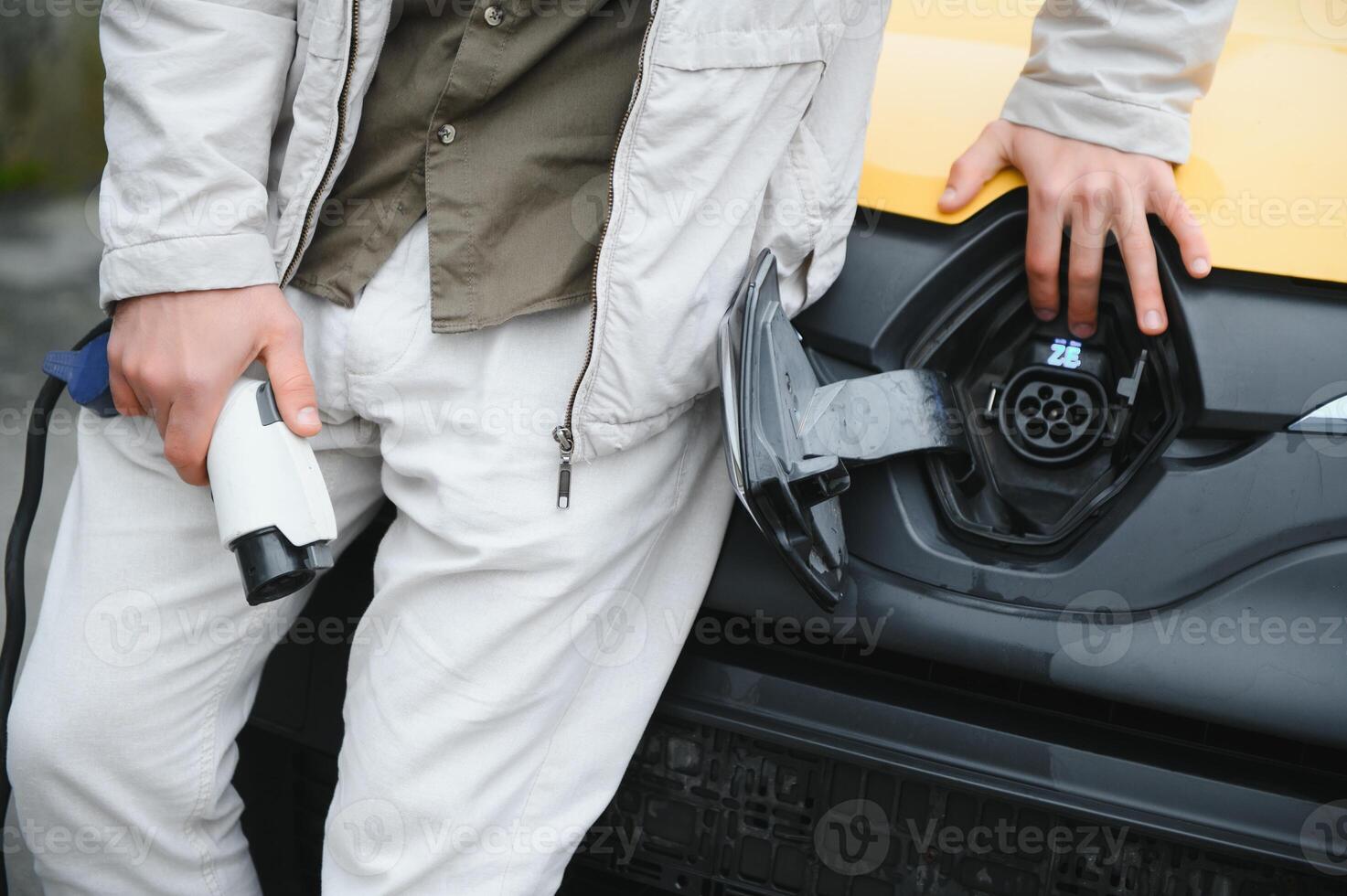 Portrait of a young man standing with charging cable near the charging station photo