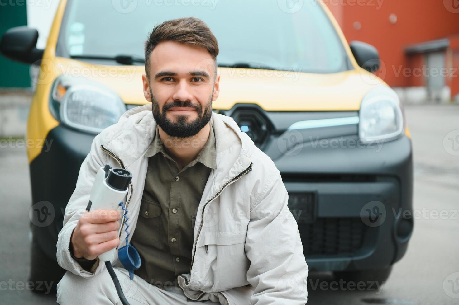 Man Holding Power Charging Cable For Electric Car In Outdoor Car Park. And he s going to connect the car to the charging station in the parking lot near the shopping center photo