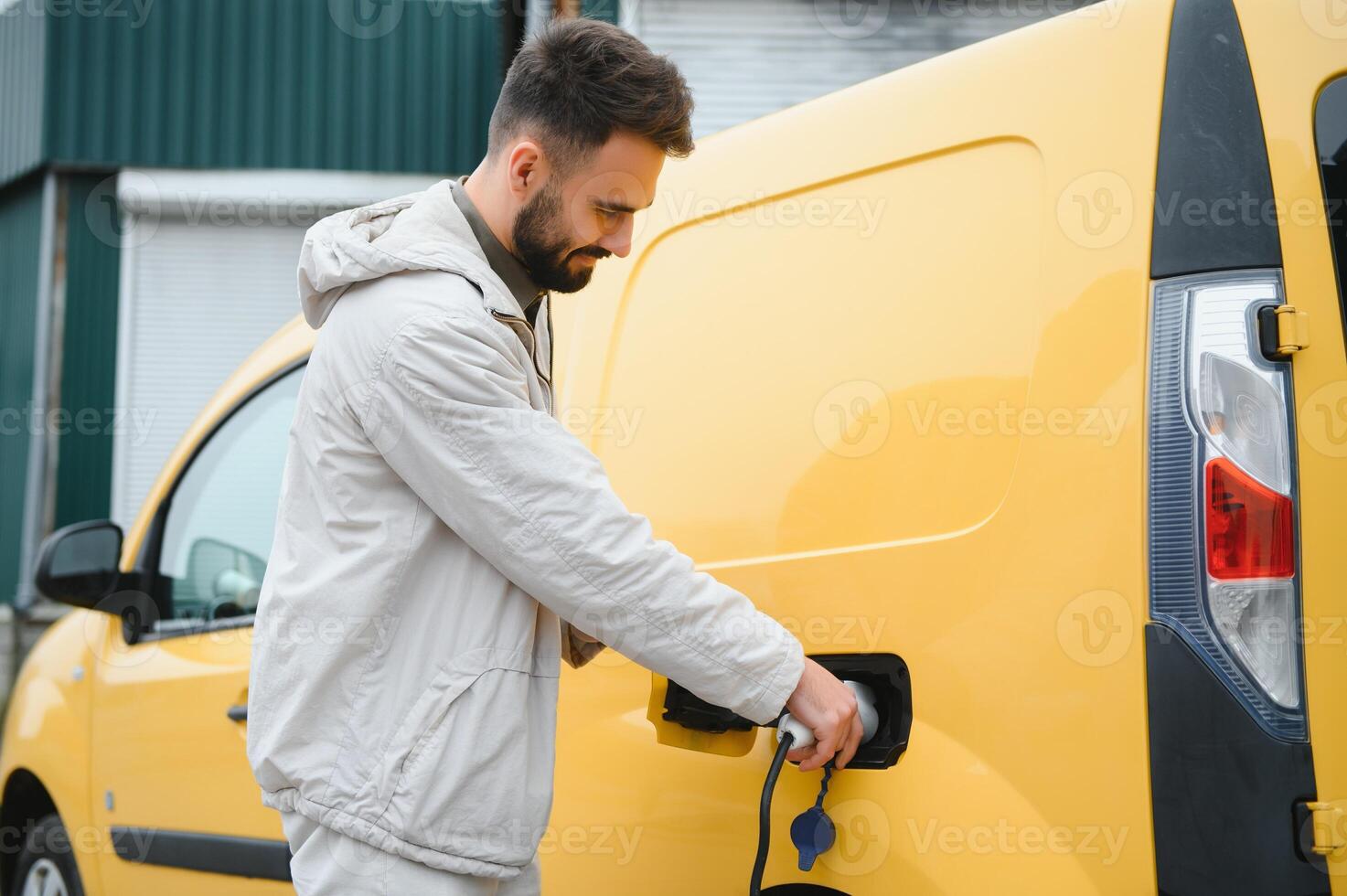 Portrait of a young man standing with charging cable near the charging station photo