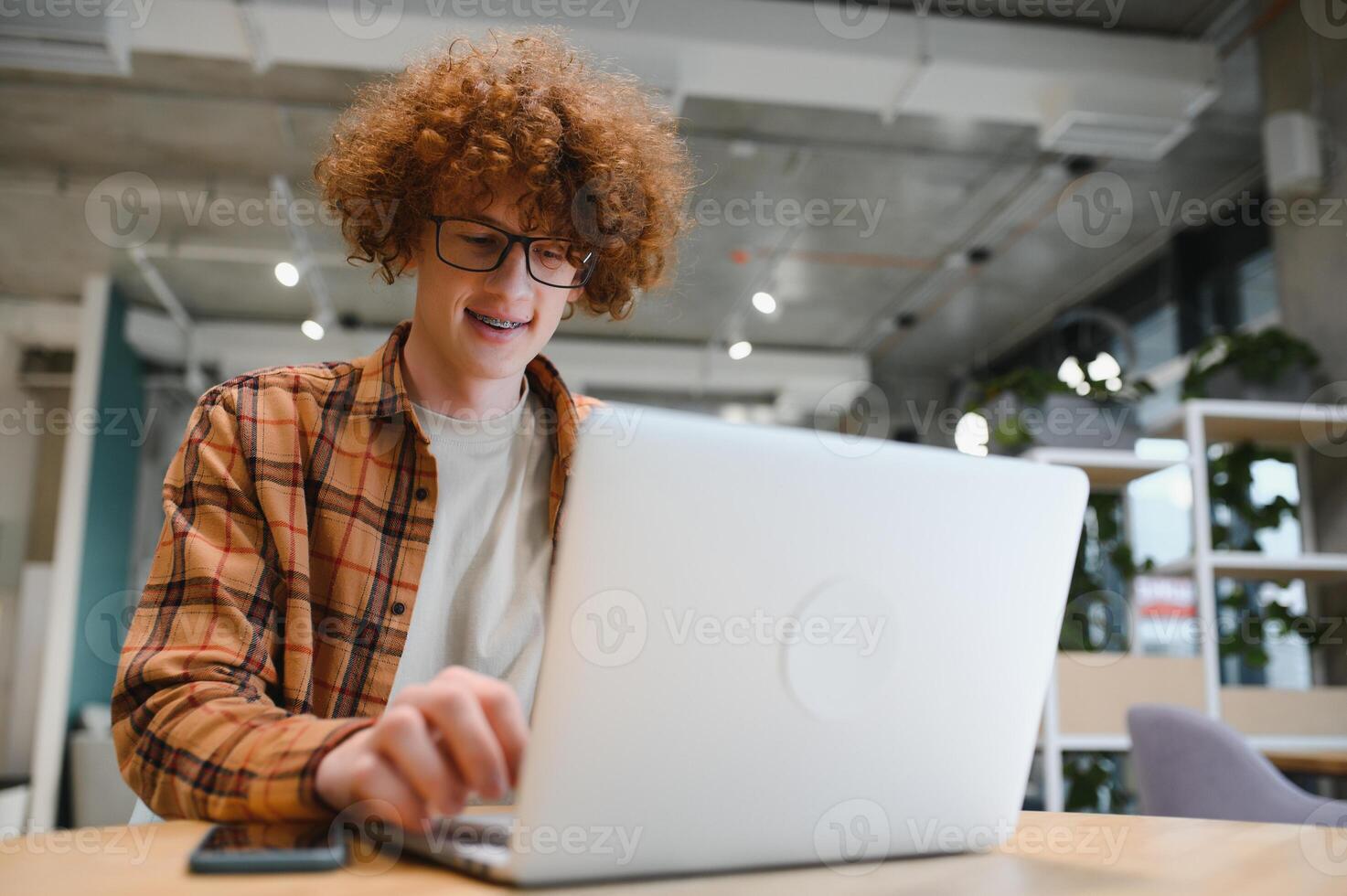 Portrait of Caucasian male freelancer in trendy apparel sitting at cafeteria table and doing remote work for programming design of public website, skilled software developer posing in coworking space. photo
