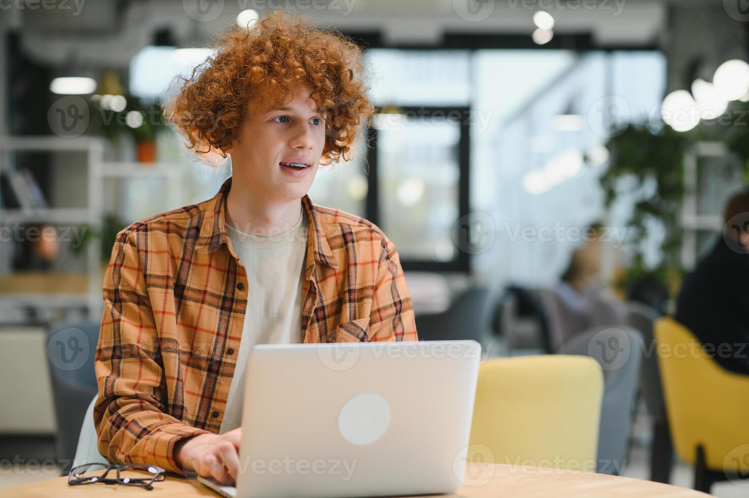 Portrait of Caucasian male freelancer in trendy apparel sitting at cafeteria table and doing remote work for programming design of public website, skilled software developer posing in coworking space. photo