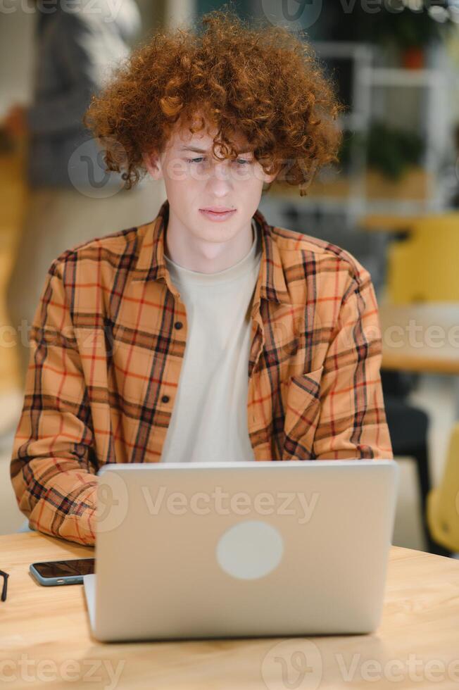 Portrait of Caucasian male freelancer in trendy apparel sitting at cafeteria table and doing remote work for programming design of public website, skilled software developer posing in coworking space. photo