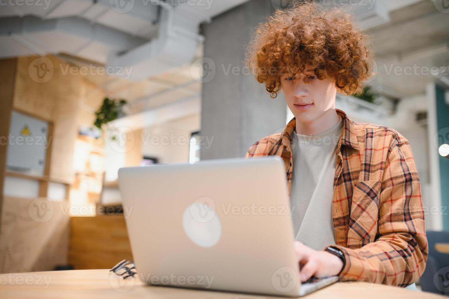 Portrait of Caucasian male freelancer in trendy apparel sitting at cafeteria table and doing remote work for programming design of public website, skilled software developer posing in coworking space. photo