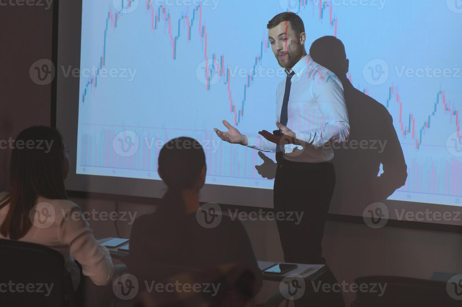 Young Businessman Explaining Graphs To His Colleagues On Projector photo