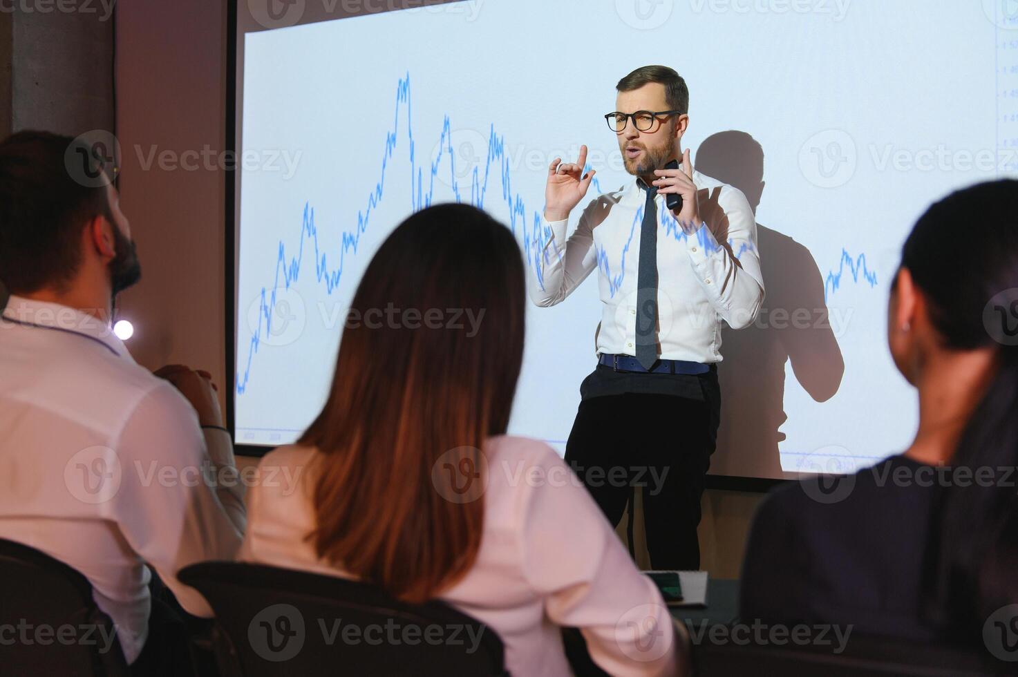 Trading teaching. Male leader talking to employees, showing the plan on the projector in office of stock exchange company. photo