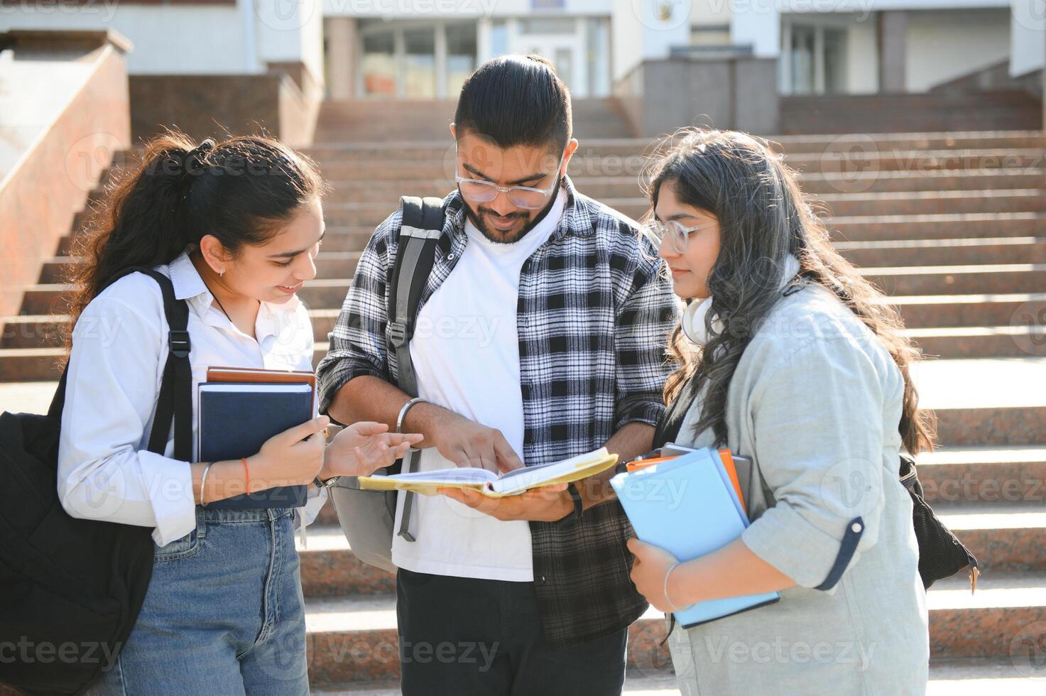 Three international students standing and holding a books photo