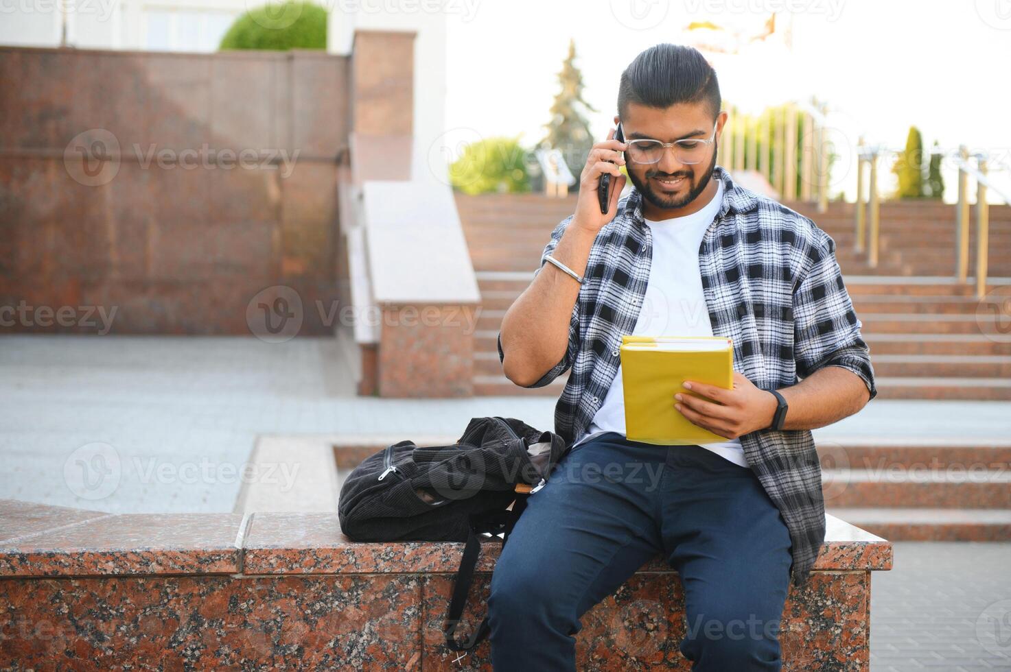 Young Indian male student using mobile phone, standing outside on street photo