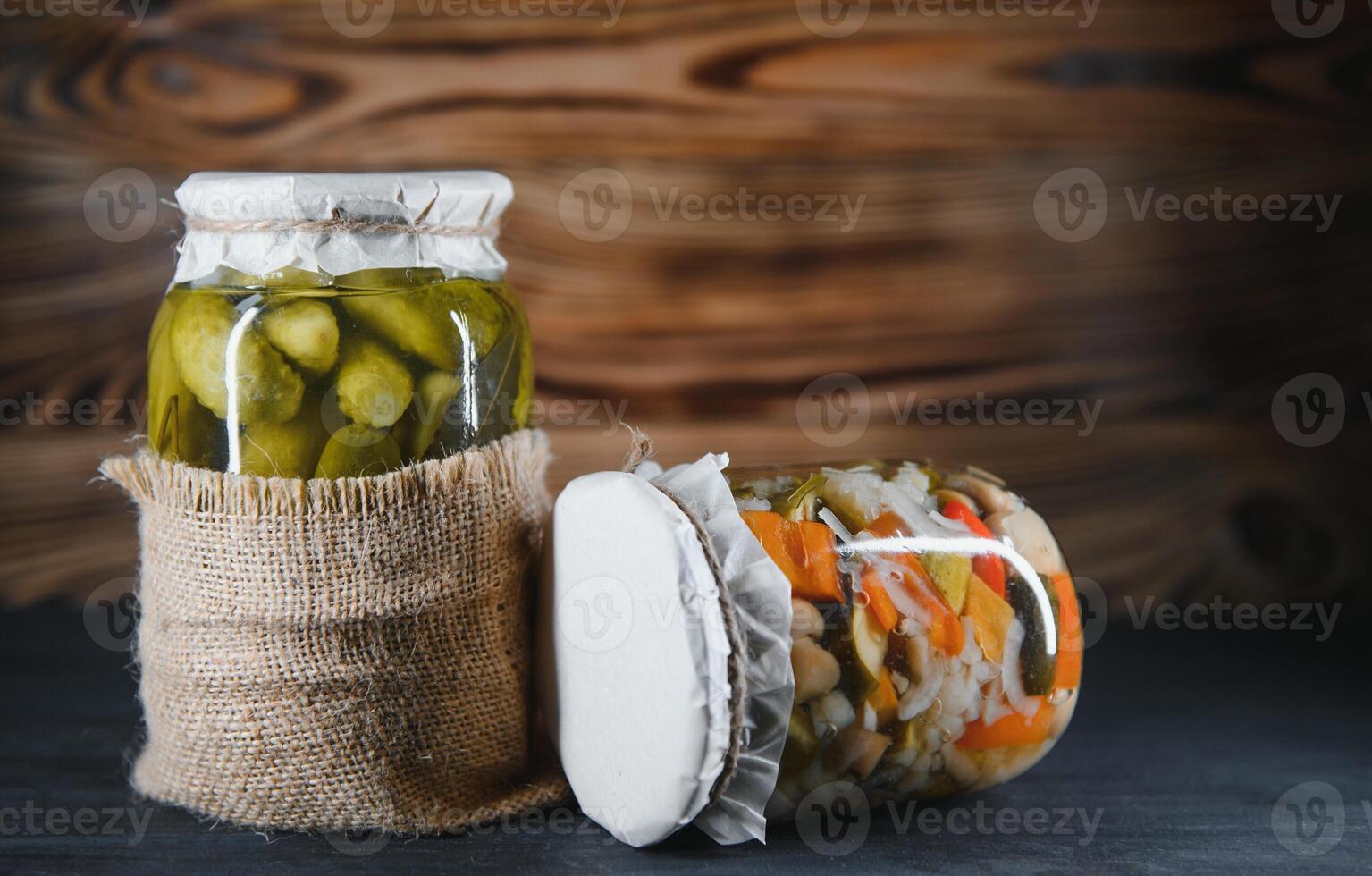Canned cucumbers and tomatoes with craft lids on a wooden background. Cucumbers and tomatoes with place for text. Stocks of canned food. Harvest, stocks for the winter. photo